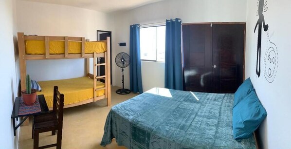 Cozy bedroom with a bunk bed and single bed, a desk with chair, and a potted plant.