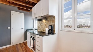 Cozinha compacta com painel de pedra, cafeteira e vista para a cidade através de uma janela.