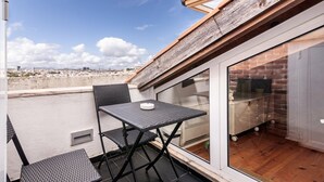 Terraço no telhado com mesa e cadeiras, porta de vidro que dá para um interior de tijolos e vista da cidade.