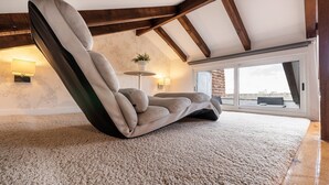Uma sala de estar moderna com um sofá grande e confortável, uma mesinha de apoio com abajur, e vista para a cidade através de janelas amplas.