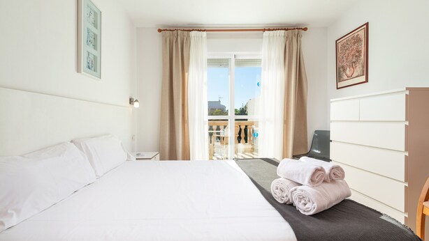 A hotel room with a large bed, a desk, a chair, a window with curtains, and a view of the outside. - Sunset Villa El Olivo (Alcúdia)