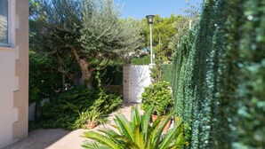 A courtyard with a variety of plants, a lamp post, and a white wall. - Sunset Villa El Olivo (Alcúdia)