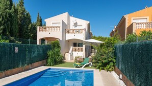 A swimming pool with a clear blue water, surrounded by a hedge and a building with a balcony. - Sunset Villa El Olivo (Alcúdia)