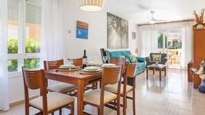 A dining area with a wooden table set for four, surrounded by chairs. There is a sofa and a small coffee table in the background. - Sunset Villa El Olivo (Alcúdia)