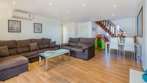 A spacious living room with a brown sectional sofa, a glass coffee table, and a staircase leading to a dining area. - Sunset Villa Isleta (Alcúdia)