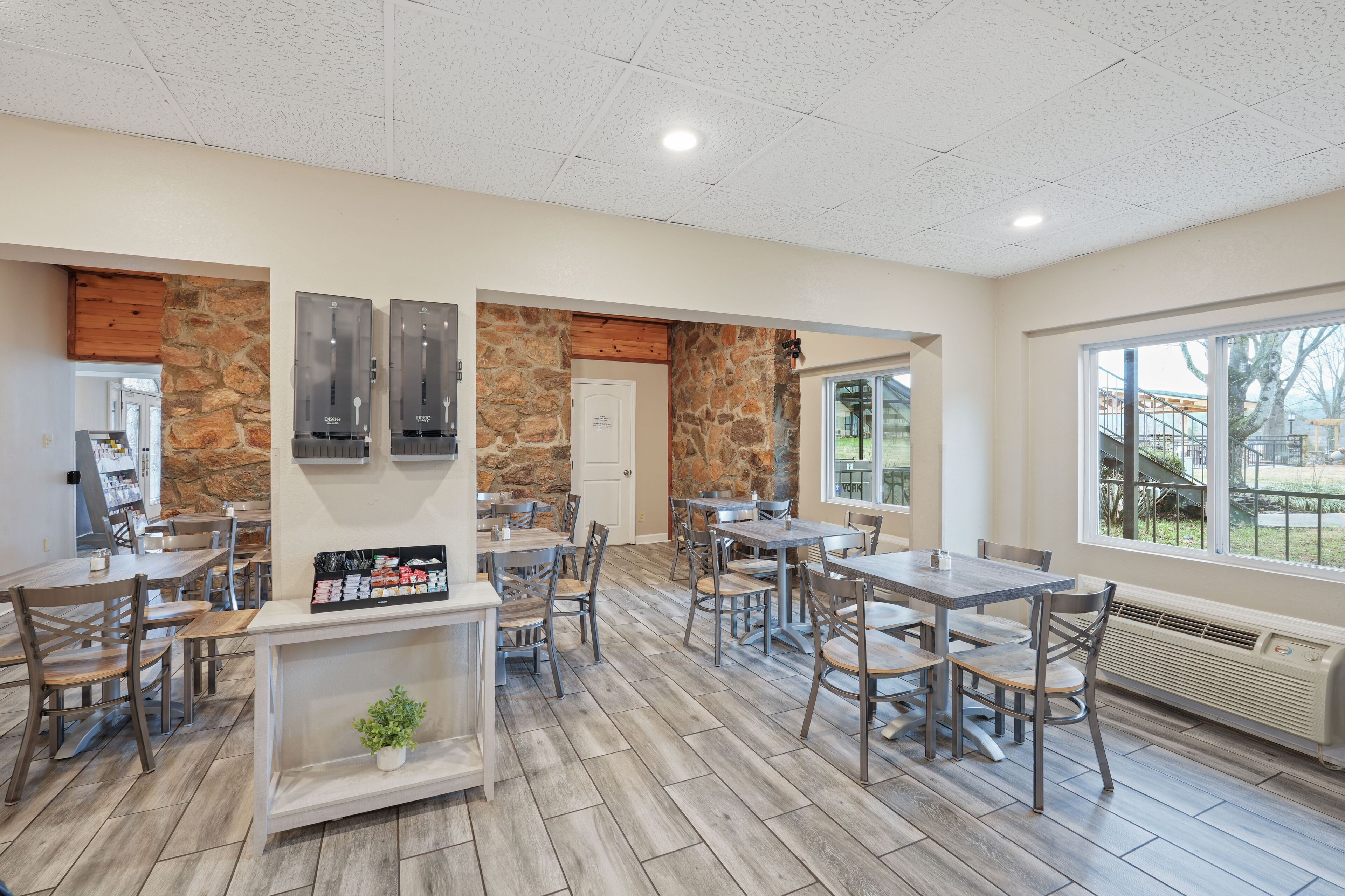 A spacious indoor area with wooden flooring, stone walls, and multiple tables and chairs.