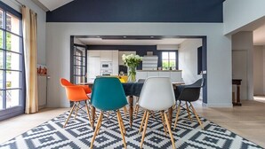 Uma área de jantar moderna com um tapete estampado em preto e branco, uma mesa central com cadeiras e vista para a cozinha.