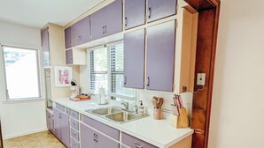 Keittiössä on violetit kaapit, valkoinen työtaso ja ikkuna, jossa on sälekaihtimet.