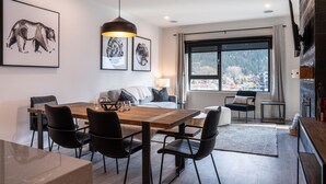 A modern living room with a wooden dining table, black chairs, and a large window offering a city view. - Altitude Adjustment Revelstoke Vacations (Revelstoke)