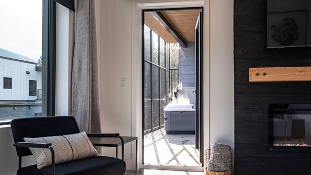 A modern interior with a black chair, a fireplace, and a view of a hot tub outside. - Altitude Adjustment Revelstoke Vacations (Revelstoke)
