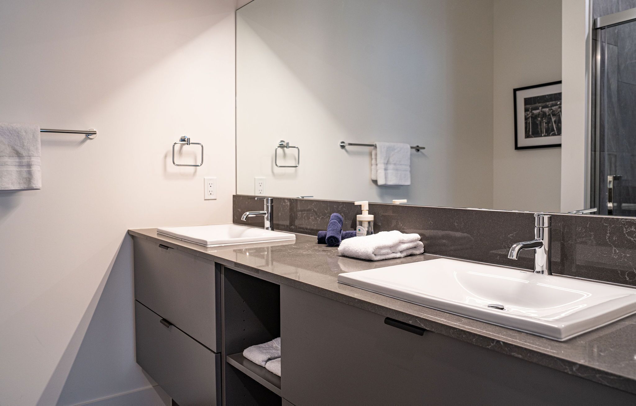 A modern bathroom with two sinks, a large mirror, and a towel rack.