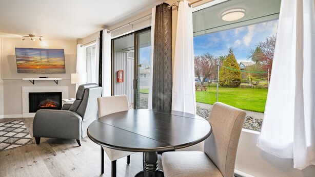 A modern living room with a fireplace, comfortable seating, a dining table, and a large window offering a view of a green landscape.