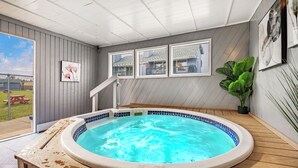 A hot tub in a room with a view of a house, a staircase, and a potted plant.