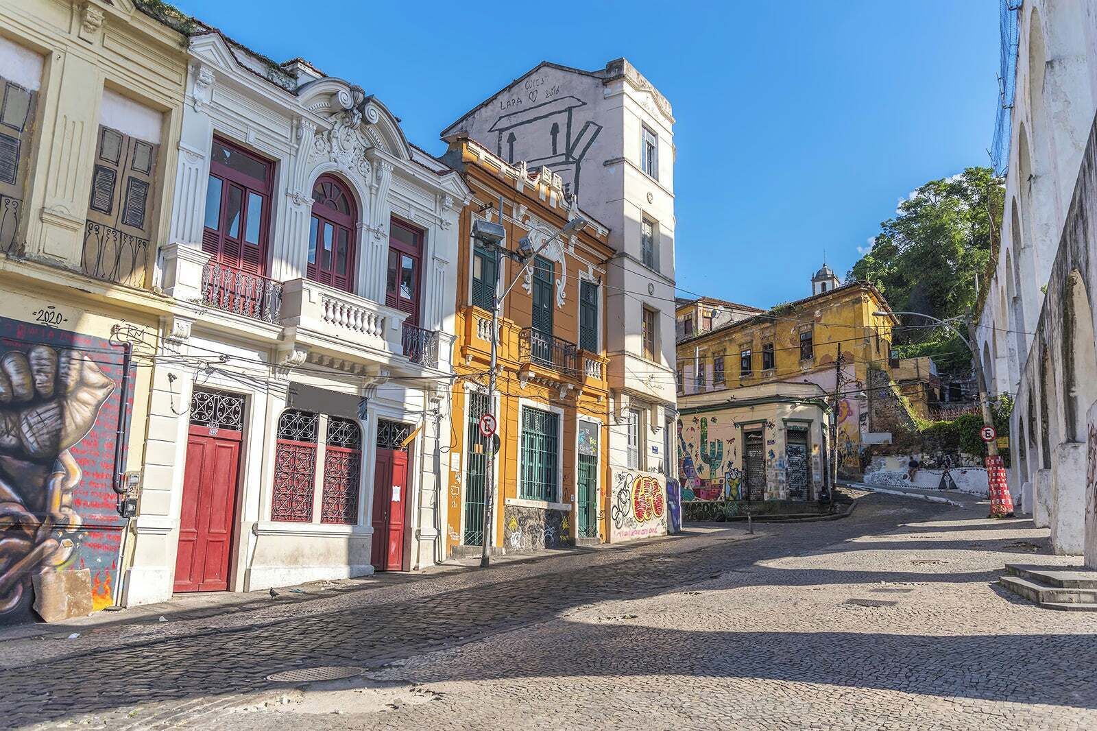 Rua de paralelepípedos ladeada por edifícios coloridos, alguns com varandas e detalhes decorativos.