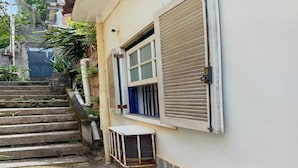 A residential building with a staircase leading to a window with a shutter, a small window with a metal grille, and a concrete wall.