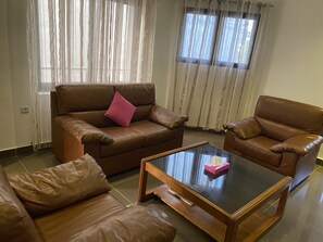 Uma sala de estar com um sofá de couro marrom, uma poltrona combinando e uma mesa de centro de vidro.
