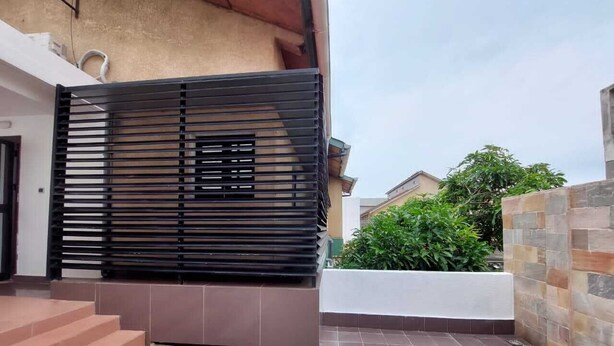 A modern outdoor patio area with a black metal fence, a white planter, and a green chair. - Cozyapartment (Cotonou)