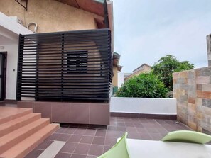 Un patio exterior moderno con una valla de metal negro, una maceta blanca y una silla verde.