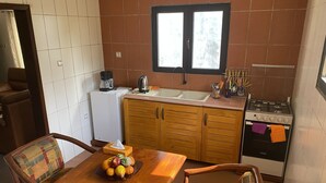 A compact kitchen with a dining table, chairs, a refrigerator, a stove, and a window above the sink. - Cozyapartment (Cotonou)