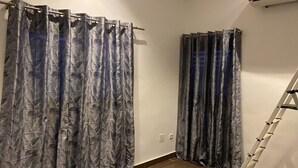 A bathroom with two shower curtains featuring a leaf pattern, a white wall, a white floor, and a white ladder leaning against the wall. - Cozyapartment (Cotonou)