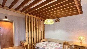 Un coin repas avec une table et des chaises en bois, un luminaire suspendu et un petit meuble sur lequel est posée une lampe.