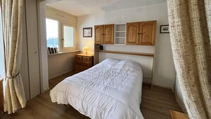 Une chambre à coucher avec un lit, une tête de lit en bois, une table de chevet avec une lampe et une fenêtre avec des rideaux.