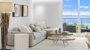 A modern living room with a large window offering a view of the sea, a sofa, a coffee table, and decorative items.