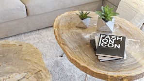 A round wooden coffee table with two potted plants and a book titled 'FASHION ICON'.