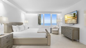 Ein modernes Hotelzimmer mit einem großen Bett, einem Fernseher, einem Schminktisch und Blick aufs Meer.