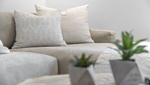 Ein sofa in neutralen Farbtönen mit gemusterten Kissen und einer Topfpflanze im Vordergrund.