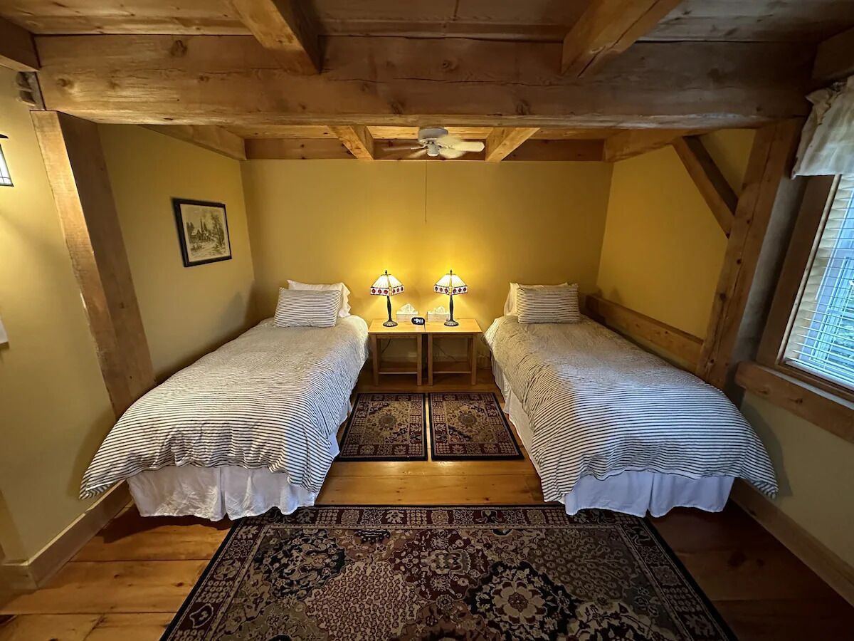 Une chambre confortable avec deux lits simples, un plafond en bois, une petite table avec des lampes et un tapis à motifs.