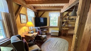 A cozy cabin interior with wooden floors, a television, a sofa, and a dining area. - The Henhouse at The Yellow Barn Estate (Freeville)
