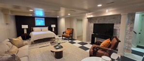 Habitación de hotel con cama, dos sillas, una mesa de centro, televisor y chimenea.