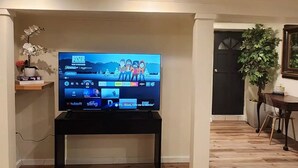 Ein Wohnzimmer mit einem Flachbildfernseher auf einem Schrank, einem gemusterten Teppich, Holzdielen und einer Tür zu einem anderen Raum.