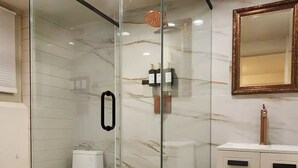 A modern bathroom with a glass-enclosed shower, a white toilet, and a marble backsplash.