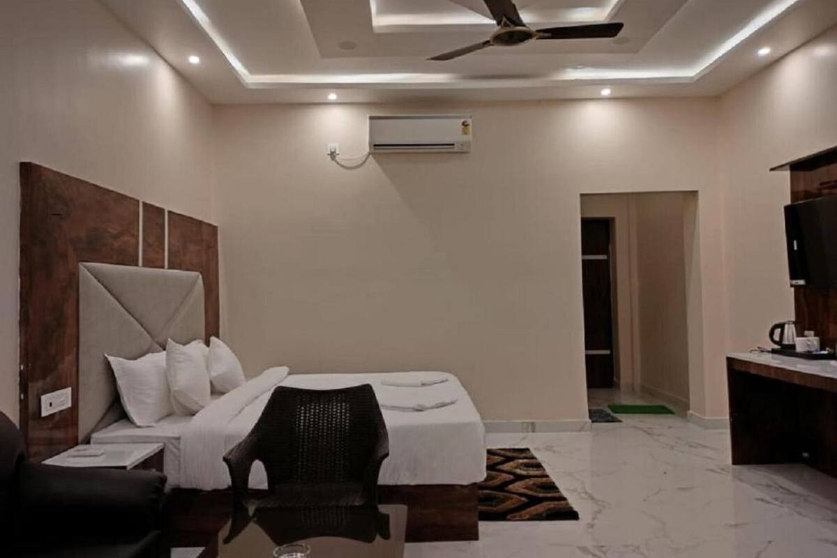 A hotel room with a bed, a chair, a small table, a ceiling fan, an air conditioning unit, and a television.