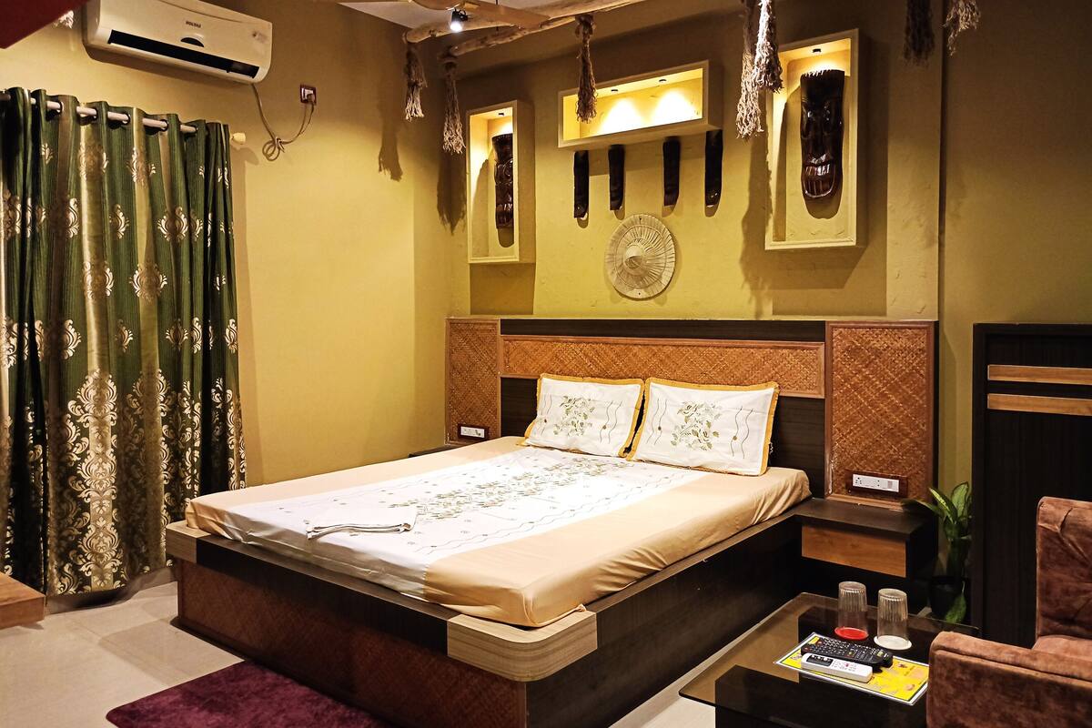 A hotel room with a bed, bedside tables, a desk, a chair, an air conditioner, and a ceiling fan.