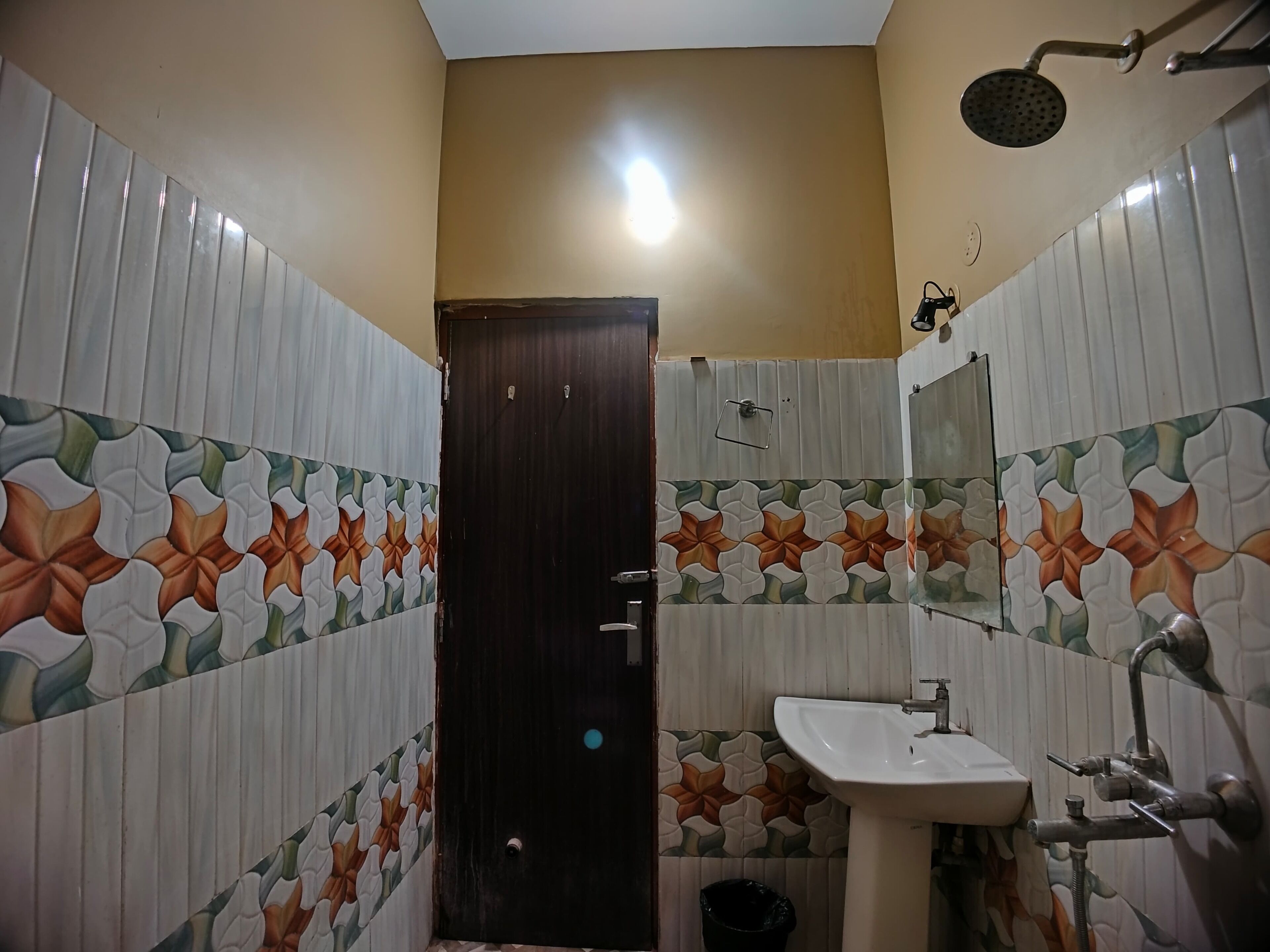 A bathroom with a tiled floor, a sink, a mirror, and a shower.