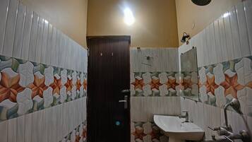 A bathroom with a tiled floor, a sink, a mirror, and a shower.