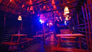 An indoor space with a thatched roof, wooden tables and benches, and hanging lamps. - The Sea Horse (Kanthi)