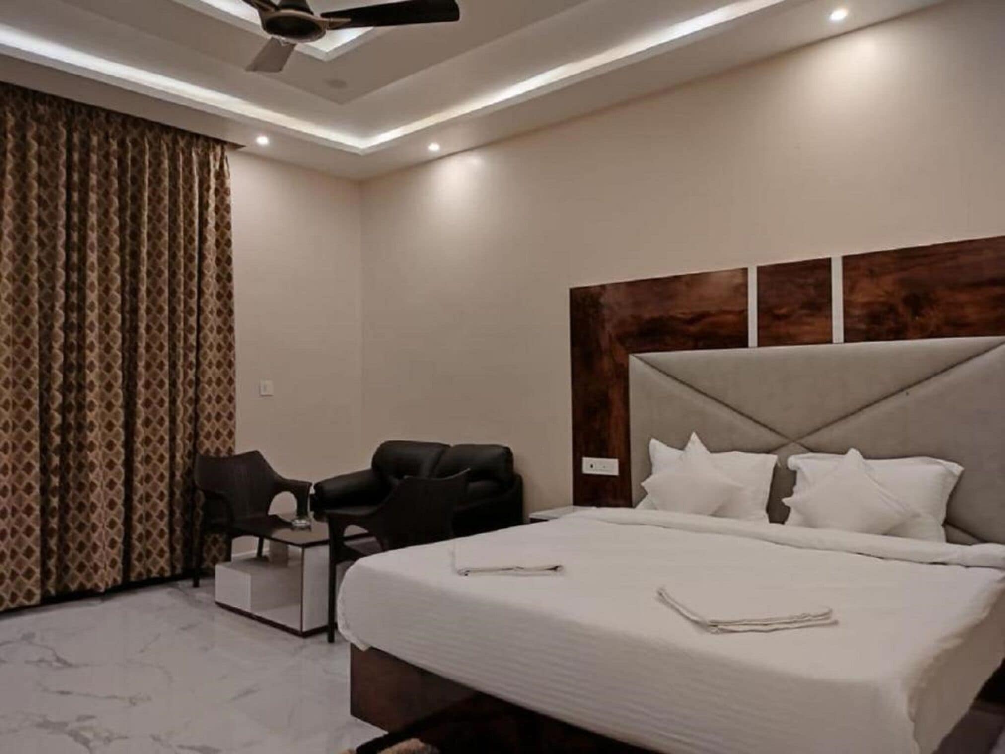 A modern hotel room with a large bed, a desk, a chair, and a ceiling fan.