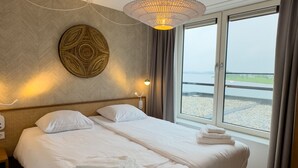 A hotel room with a large bed, a view of the water, and a decorative wall piece. - Premium Island 6p in Thorn (Thorn)