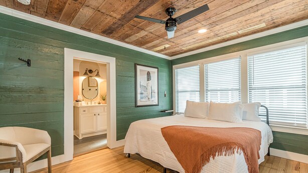 Een slaapkamer met een bed, een stoel, een kaptafel met spiegel en een plafondventilator.