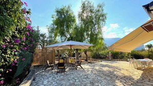 Un espace patio doté d’un sol en pierre, de mobilier d’extérieur et de parasols pour créer de l’ombre.