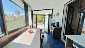 Une pièce comprenant une table à manger, des chaises, un coin cuisine et donnant sur l’extérieur.