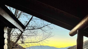 Une terrasse en bois avec deux fauteuils à bascule donnant sur un paysage montagneux au coucher du soleil.