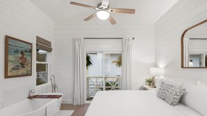 A bedroom with a large bed, a bathtub, a ceiling fan, and a balcony with a view. - Mahi Mahi Cottage in the Woods (Santa Rosa Beach)