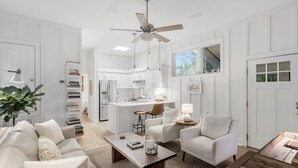A modern living room with a sofa, coffee table, and a dining area with chairs and a table. - Mahi Mahi Cottage in the Woods (Santa Rosa Beach)
