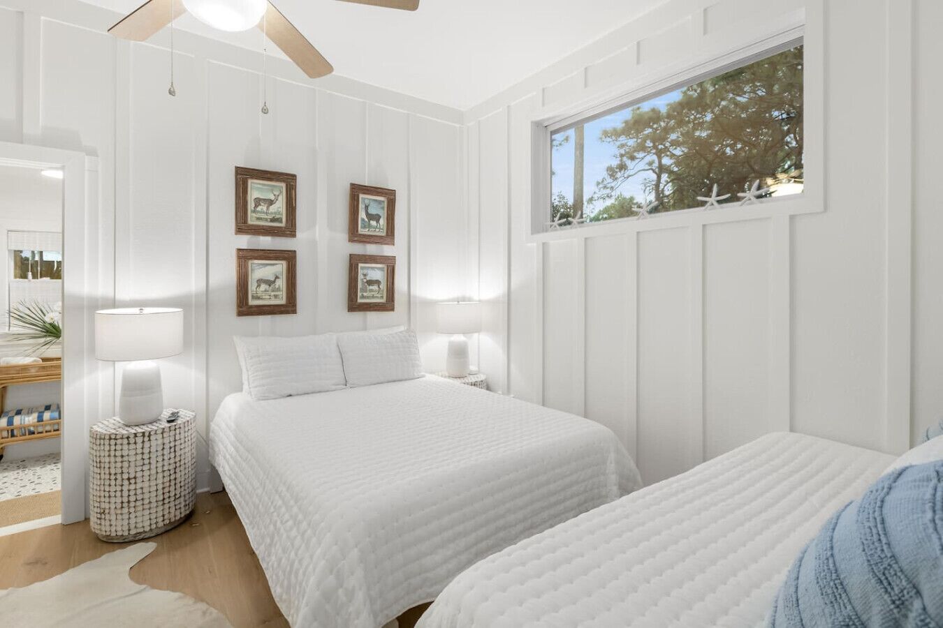 A bedroom with a large bed, two bedside tables, a ceiling fan, and a window with a view of trees.
