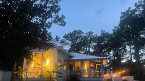 A two-story house with a porch and a covered area, surrounded by trees and a well-maintained lawn. - Mahi Mahi Cottage in the Woods (Santa Rosa Beach)